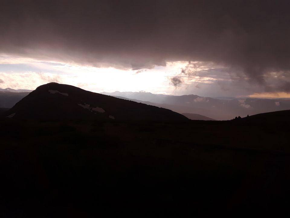 Mountain range silhouette against a dramatic sky with sunbeams breaking through clouds