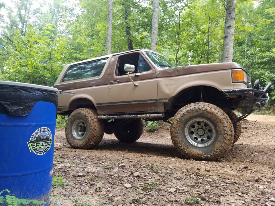 Lifted Ford Bronco on a dirt road, next to a blue barrel