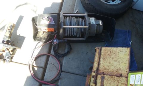 1995 Ford Bronco - A winch and its associated parts are laid out on a paved surface next to a tire.