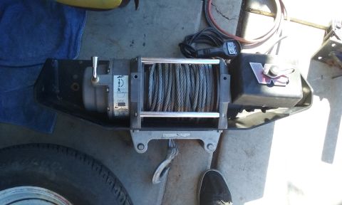 1995 Ford Bronco - A winch with a steel cable and a red logo is shown, mounted on a bracket.
