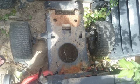 1995 Ford Bronco - The rusted frame and wheels of a lawn mower sit on the ground amidst some foliage.