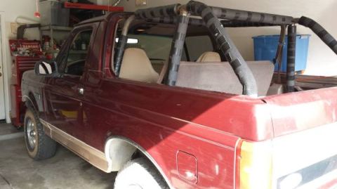 1996 Ford Bronco - The side profile of a red SUV with a roll cage is visible in a garage setting.