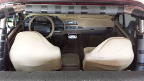 1996 Ford Bronco - The interior of a red Ford Bronco shows tan seats and dashboard, with a roll cage installed.