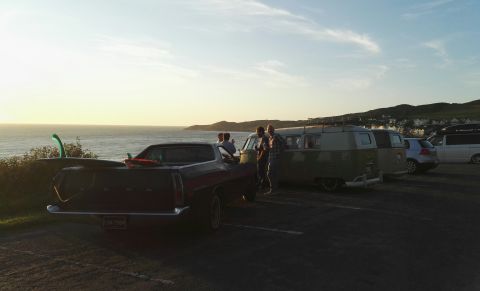 1974 Ford Ranchero - A group of people and vehicles gather near the coast at sunset, with surfboards ready for the waves.