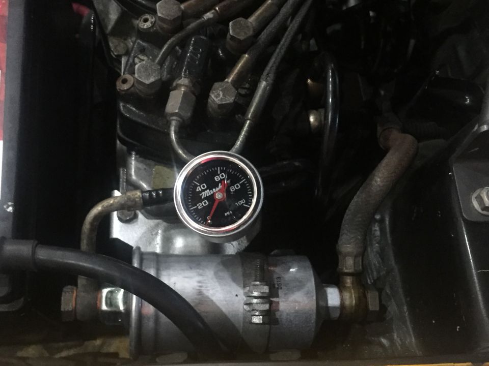 Fuel pressure gauge with red needle on 0 psi, connected to engine components