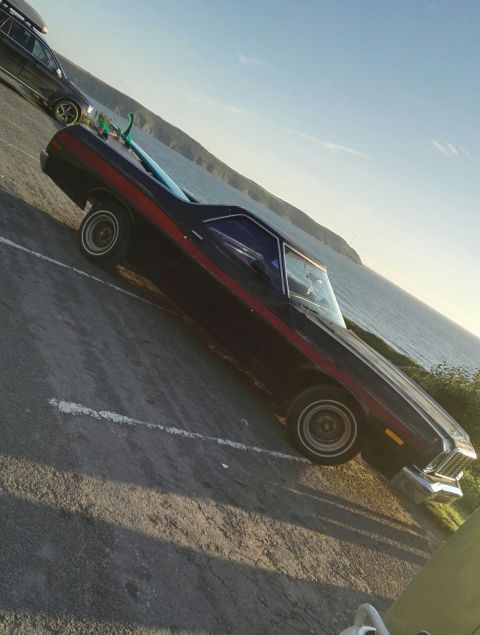 1974 Ford Ranchero - This 1974 Ford Ranchero is parked near the water, with a surfboard on its bed and a roof rack on another vehicle behind it.