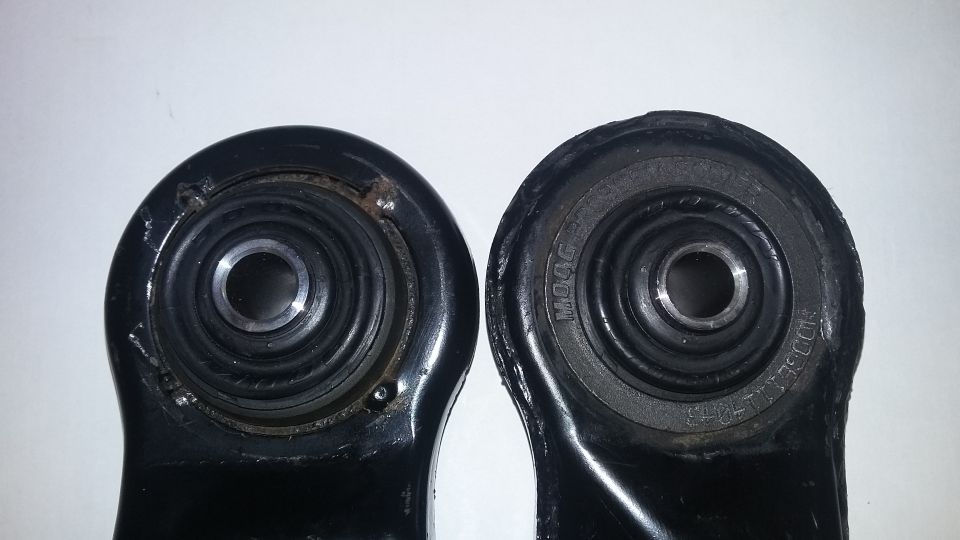 Two black suspension control arm bushings, one with visible MOOG branding and part numbers, the other showing wear and rust