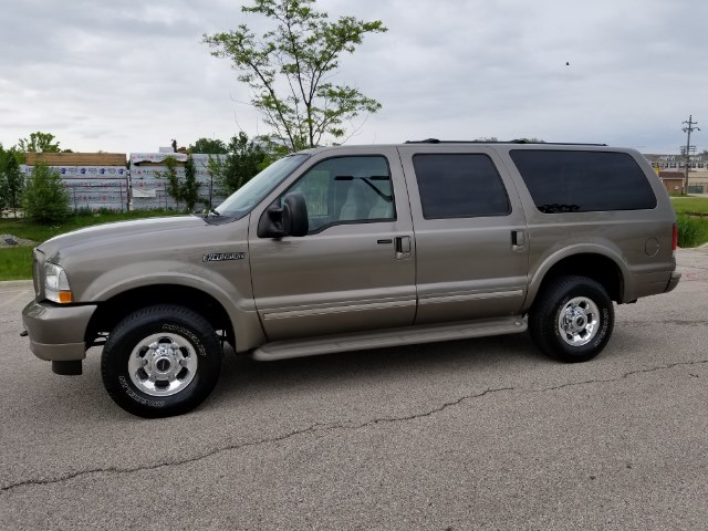 Tan Ford Excursion SUV parked on asphalt, side view. Chrome wheels, tinted windows
