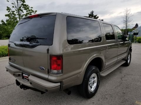 2003 Ford Excursion - The rear-right quarter of a tan 2003 Ford Excursion SUV is visible, parked outdoors on an asphalt surface.
