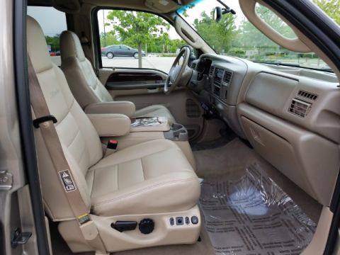 2003 Ford Excursion - The interior of a large SUV shows tan leather seats, dashboard, and floor mats, with a steering wheel in view.