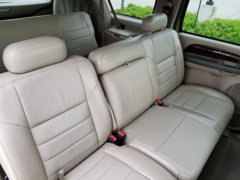 2003 Ford Excursion - The interior of a vehicle shows beige leather seats and an armrest.