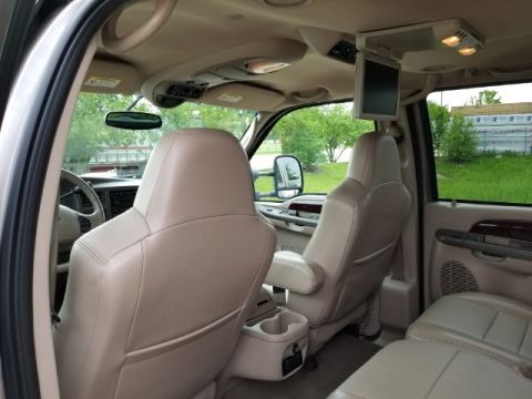 2003 Ford Excursion - The interior of a large SUV features leather seats, an overhead entertainment system, and a view of the exterior through the windows.