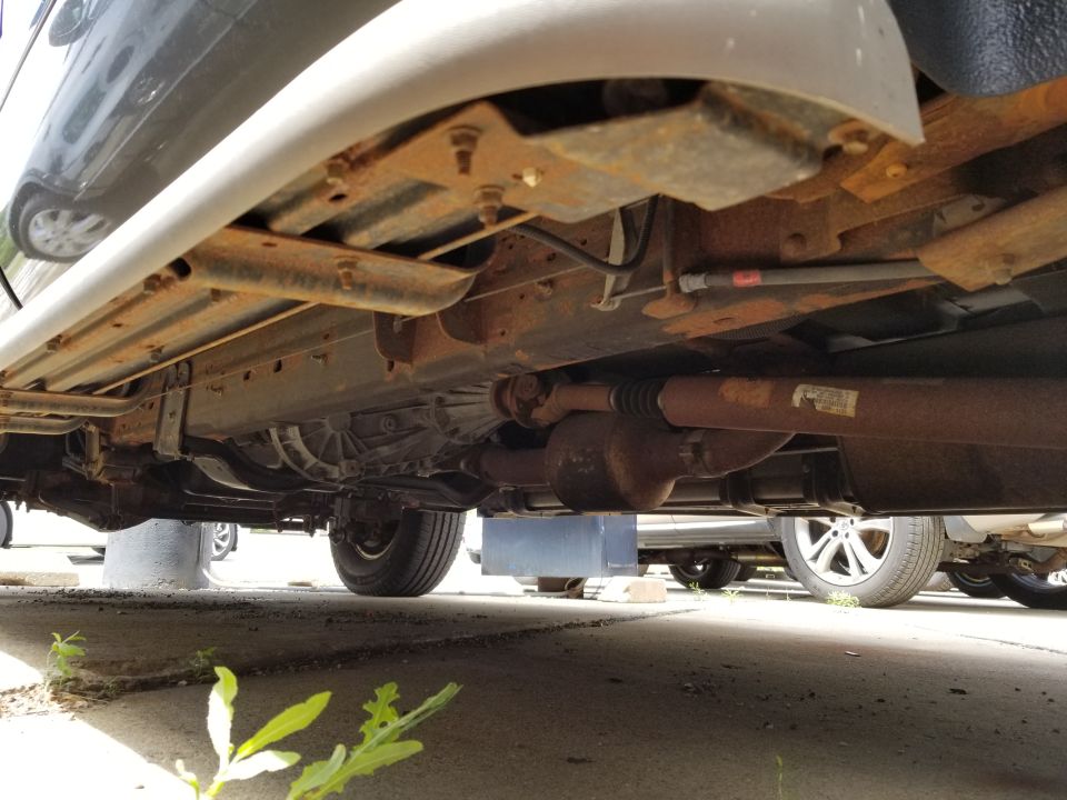 Undercarriage view of a large SUV with visible rust and exhaust system