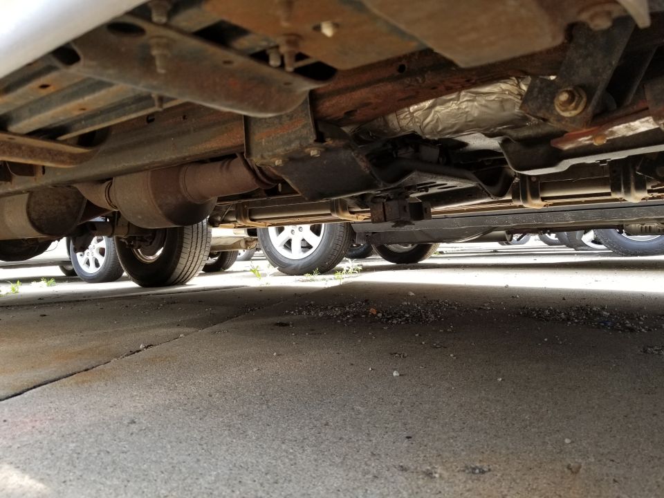 Undercarriage of several vehicles parked on asphalt, showing exhaust systems and wheels