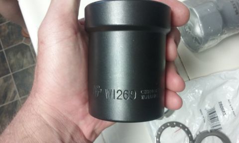 1995 Ford Bronco - A hand holds a black metal socket with "W1269 CHROME VANADIUM" stamped on it. In the background, a plastic-wrapped part with a barcode and…
