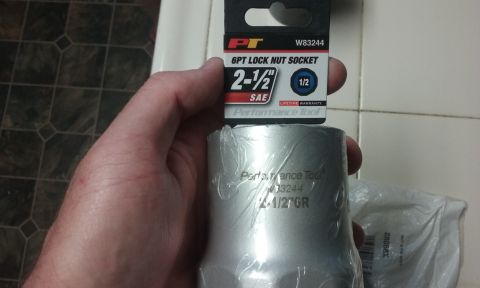 1995 Ford Bronco - A hand holds a Performance Tool 2-1/2 inch SAE 6pt lock nut socket with a 1/2 inch drive. The socket is silver and wrapped in plastic.