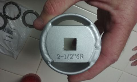 1995 Ford Bronco - A hand holds a silver metal tool with a square opening in the center, marked with "2-1/2"6R". In the background, several metal rings and a…