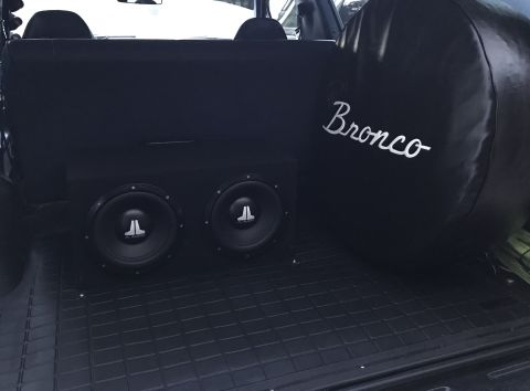 1995 Ford Bronco - The rear cargo area of a black Ford Bronco features a custom subwoofer box with two JL Audio speakers and a black spare tire cover with whi…