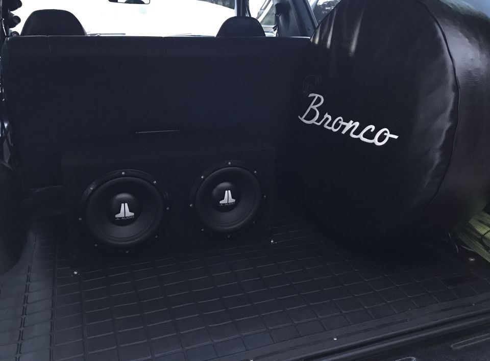 Black Ford Bronco cargo area with dual JL Audio subwoofers and a Bronco spare tire cover.