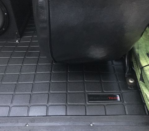 1995 Ford Bronco - A close-up view of a black WeatherTech floor mat inside a vehicle, with a portion of a black leather seat visible above it. The mat has a g…