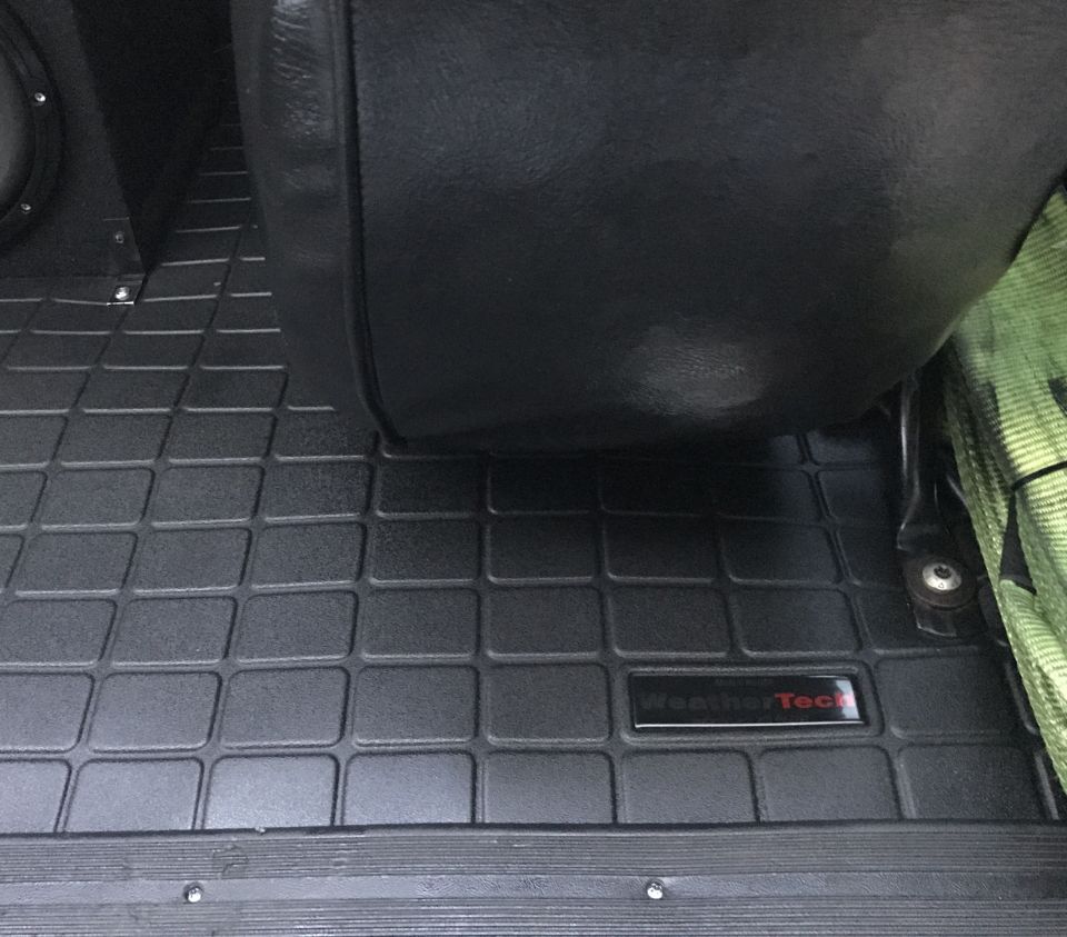 Black WeatherTech floor mat with grid pattern and logo, next to a black leather seat.
