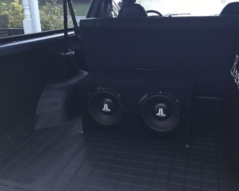1995 Ford Bronco - The rear cargo area of a dark-colored SUV features a custom subwoofer box with two JL Audio subwoofers. The floor is covered with a black r…