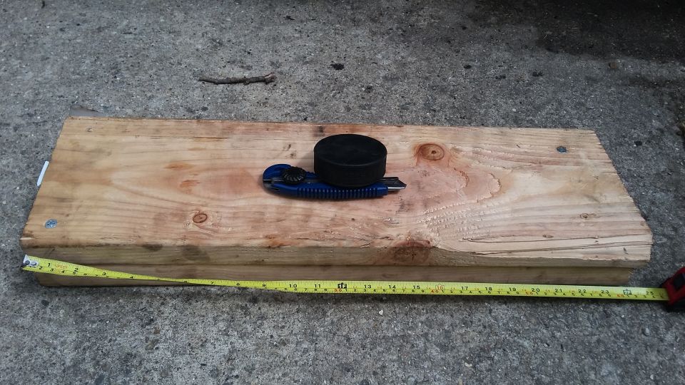 Utility knife and black puck on a wooden plank with a measuring tape.