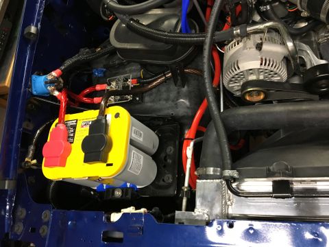 1996 Ford Bronco - The engine bay of a blue 1996 Ford Bronco shows a yellow Optima battery with red and black terminal covers, connected to a blue distributio…