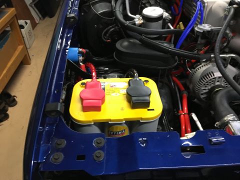 1996 Ford Bronco - The engine bay of a blue 1996 Ford Bronco shows a yellow Optima battery with red and black terminal covers, surrounded by various engine co…