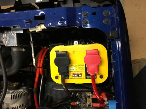 1996 Ford Bronco - A close-up view of a yellow Optima battery installed in the engine bay of a blue vehicle. The battery has red and black terminal covers and…