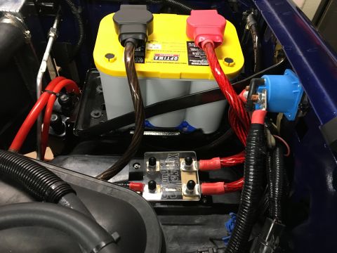 1996 Ford Bronco - A close-up view of a vehicle's engine bay shows a yellow Optima AGM battery with red and black terminal covers, connected to a blue power d…