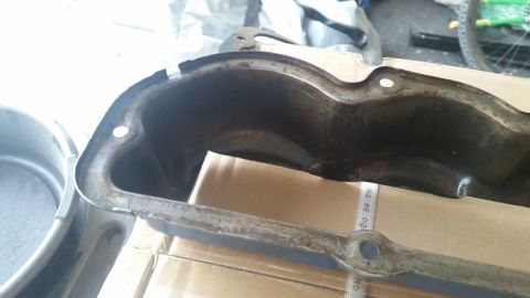 1981 Ford Bronco - A close-up, angled view of a dirty and rusty black metal part, possibly an oil pan or valve cover, resting on cardboard boxes. The part has…