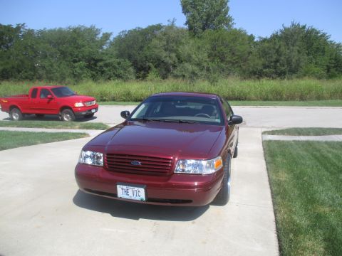 2004 Ford Crown Victoria - A maroon Ford Crown Victoria is parked on a concrete driveway in front of a red Ford F-150 pickup truck. The Crown Victoria has a license p…