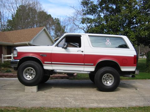 1993 Ford Bronco - This lifted 1993 Ford Bronco has a two-tone red and white paint scheme and is parked on a concrete driveway.
