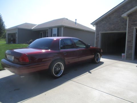2004 Ford Crown Victoria - A dark red sedan is parked on a concrete driveway in front of a house with an attached garage. The car is viewed from the rear three-quarte…