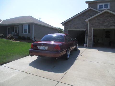 2004 Ford Crown Victoria - A maroon 2004 Ford Crown Victoria sedan is parked on a concrete driveway in front of a house with a two-car garage. The license plate reads…