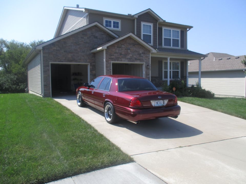 Maroon Ford Crown Victoria sedan parked in driveway in front of a house.