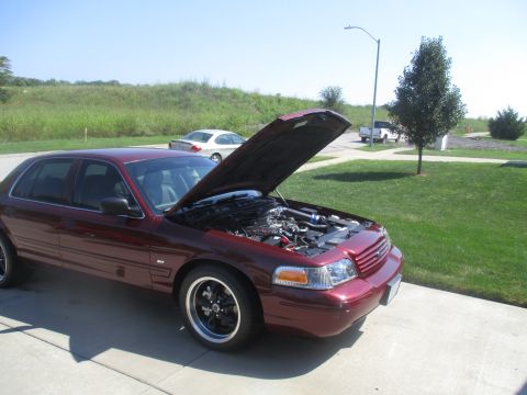 2004 Ford Crown Victoria - A maroon 2004 Ford Crown Victoria sedan is parked outside with its hood open, revealing the engine bay. The car has aftermarket black and c…