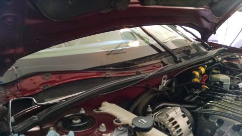2002 Pontiac Grand Prix - The hood of a dark red car is open, revealing the engine bay and the windshield area. Wires, hoses, and engine components are visible.