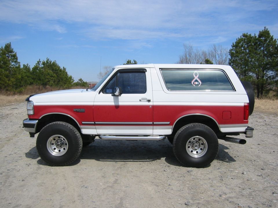 Lifted red and white 1990s Ford Bronco side view on gravel lot