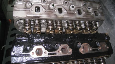 1996 Ford Bronco - Two Ford engine cylinder heads are shown, one clean and silver, the other coated in black oil. The silver cylinder head is positioned above…