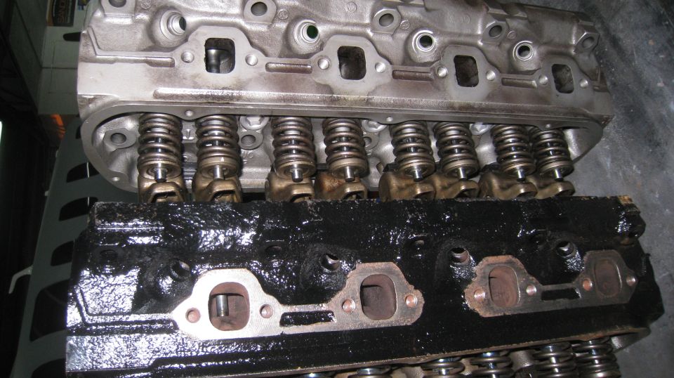 Two Ford engine cylinder heads, one clean and silver, the other black and oily.