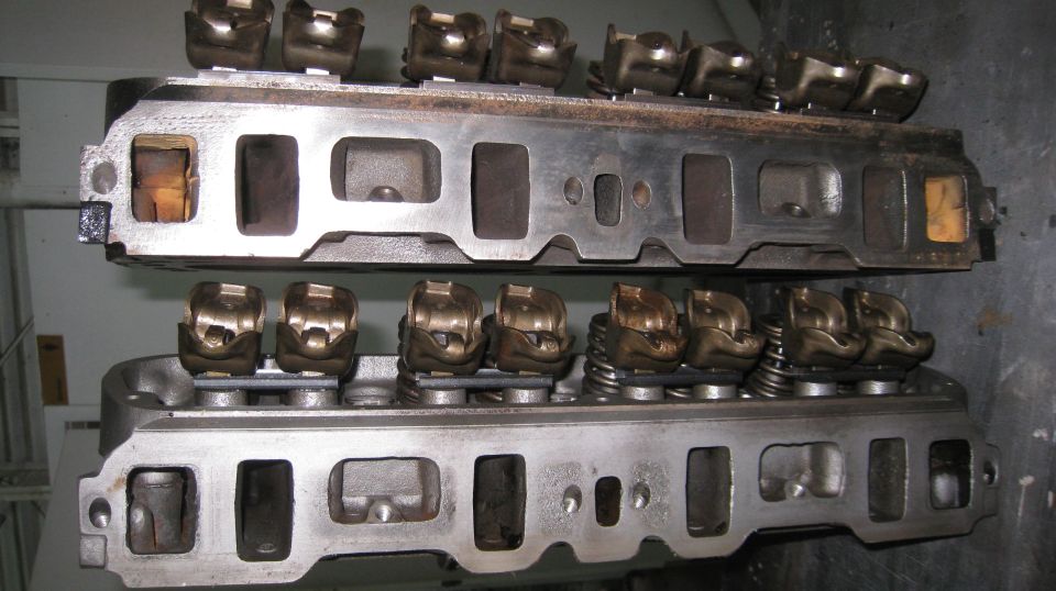 Two stacked Ford engine cylinder heads, one with visible rocker arms and valve springs.