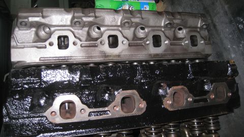1996 Ford Bronco - Two engine cylinder heads are stacked on top of each other. The top cylinder head is silver and appears to be made of aluminum, while the b…