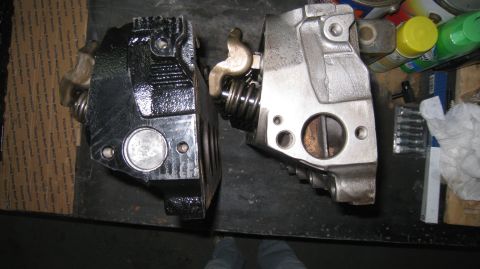 1996 Ford Bronco - Two engine cylinder heads are shown side-by-side on a dark surface. The head on the left is painted black and shows a valve spring and rock…