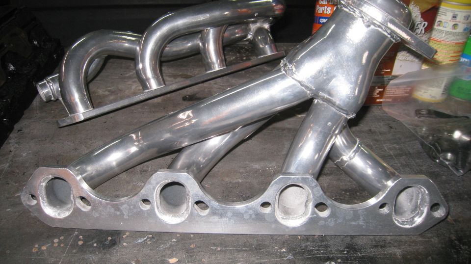 Polished aluminum exhaust manifold with four pipes merging into one, on a workbench.