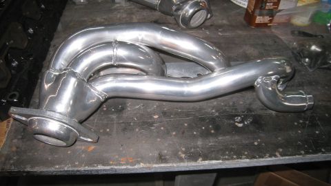 1996 Ford Bronco - A polished aluminum exhaust manifold is shown on a workbench, likely for a 1996 Ford Bronco. The manifold features multiple pipes merging i…