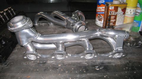 1996 Ford Bronco - A pair of polished aluminum exhaust headers are laid out on a workbench next to automotive cleaning supplies. The headers appear to be for…