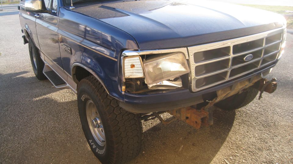 Dark blue Ford Bronco with a broken headlight and rusty bumper.