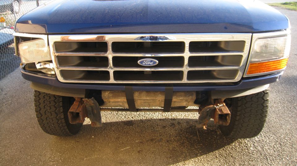 Blue 1996 Ford Bronco front view with damaged headlight and chrome grille.